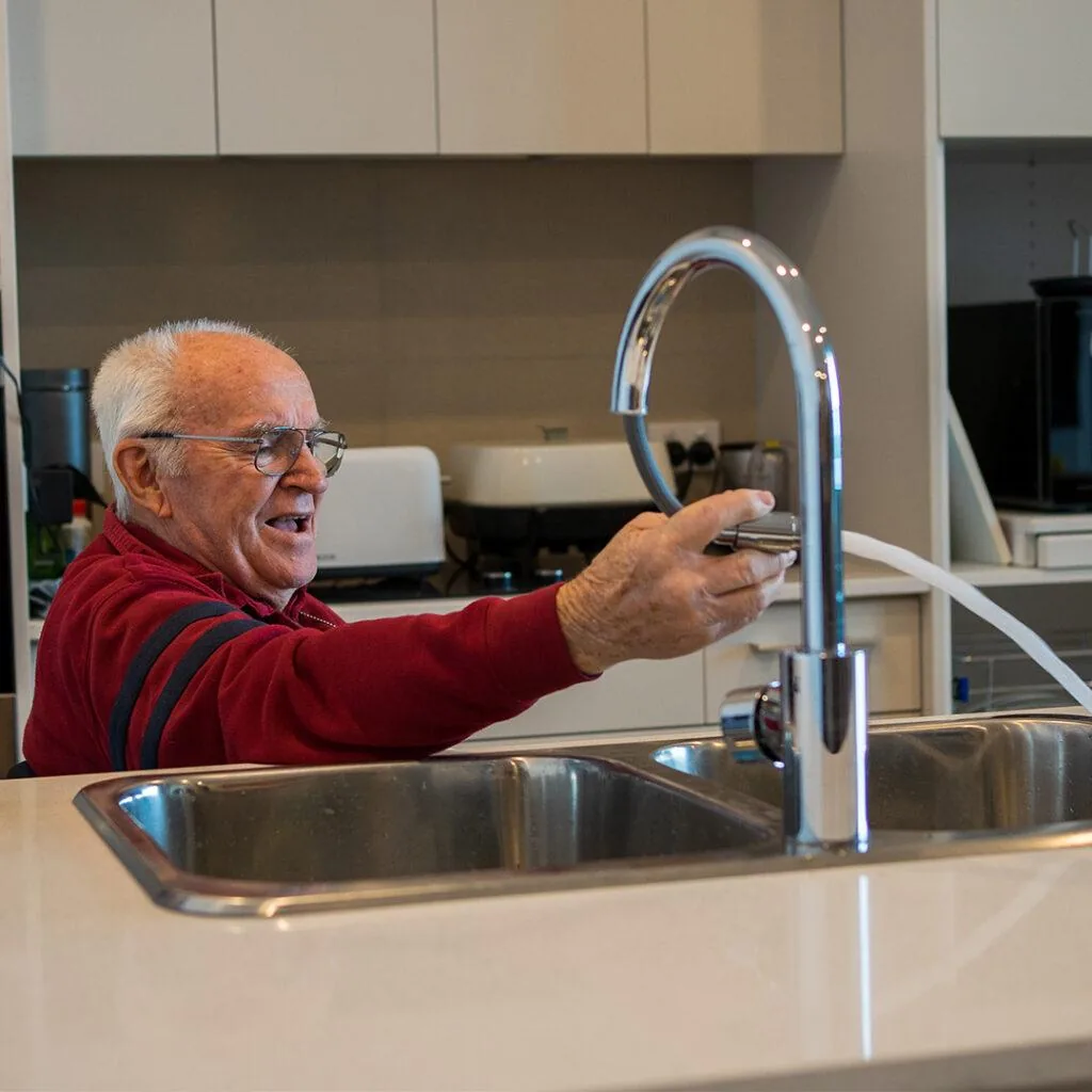 Older man using a lever-handle faucet at the kitchen sink